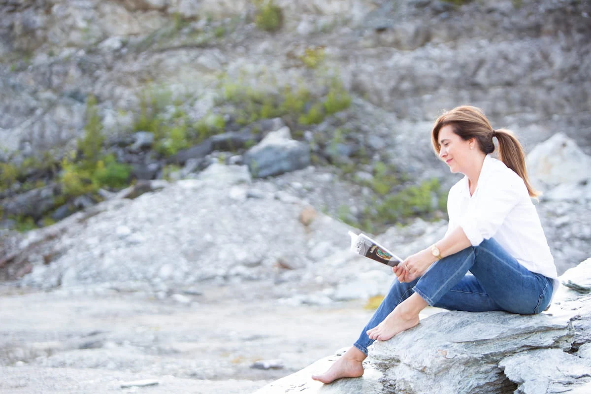 Johanne Côté assise sur un rocher, au bord de l'eau, un carnet à la main